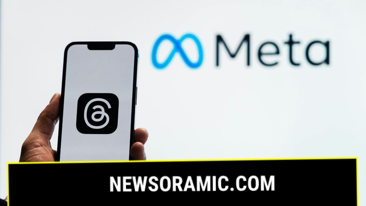 A smartphone displaying the logo of the Threads app is held in front of a screen displaying the Meta logo.