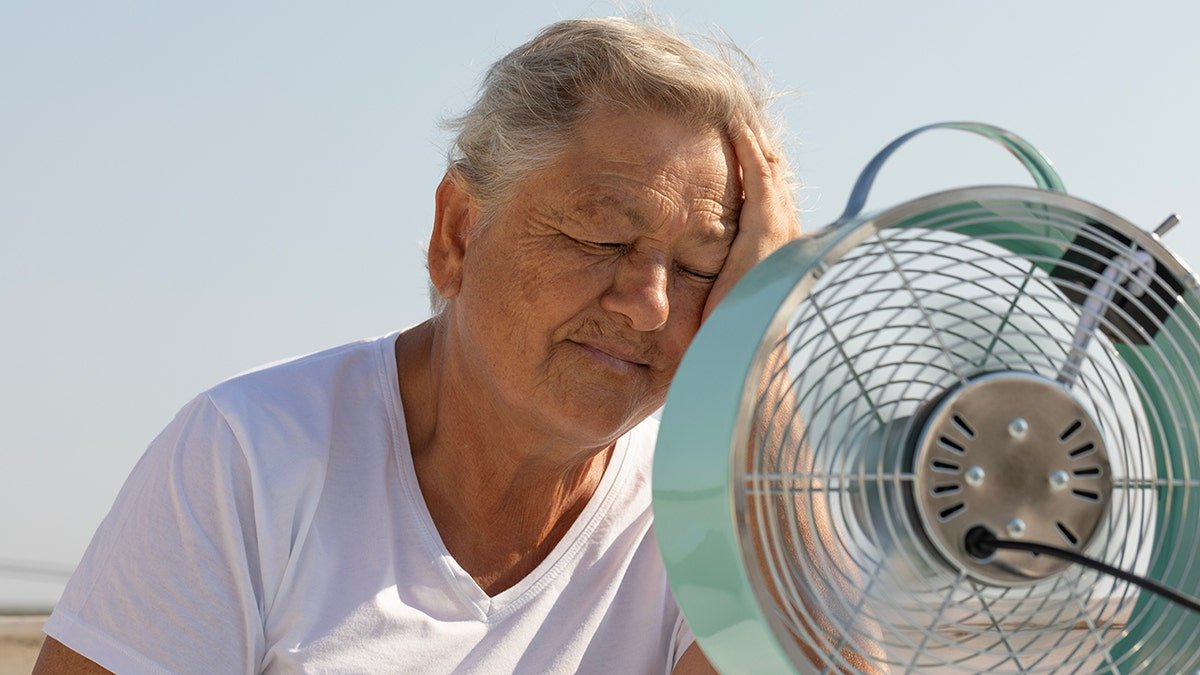 senior cools down with fan during the summer heat.