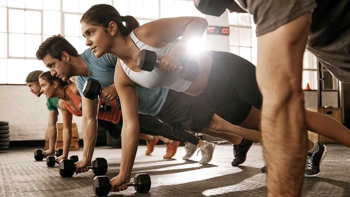 People doing exercises in a group, lifting weights in plank position