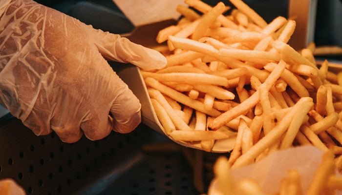 A person scoops French fries at a shop. — Unsplash