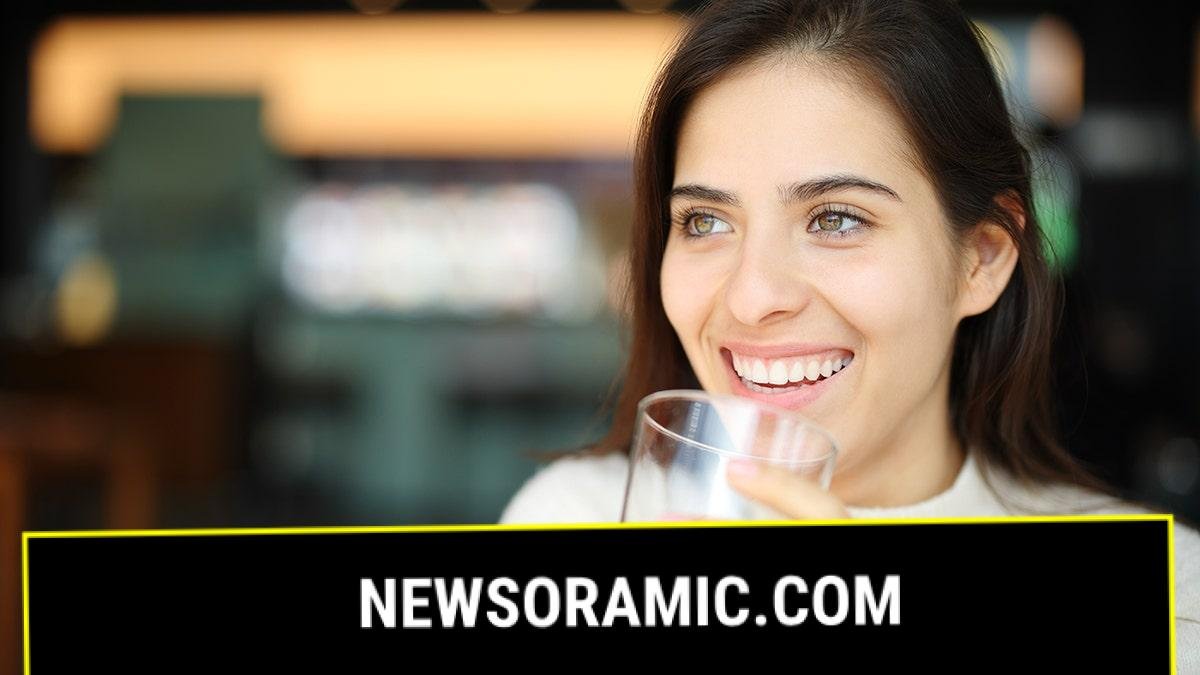 A smiling woman holds a glass of soda in her hand.