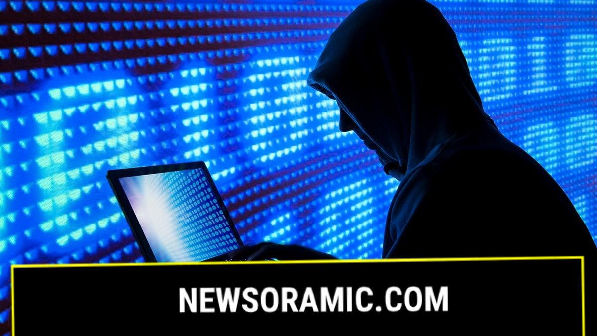 A man in a hoodie looking at a laptop against a blue screen.