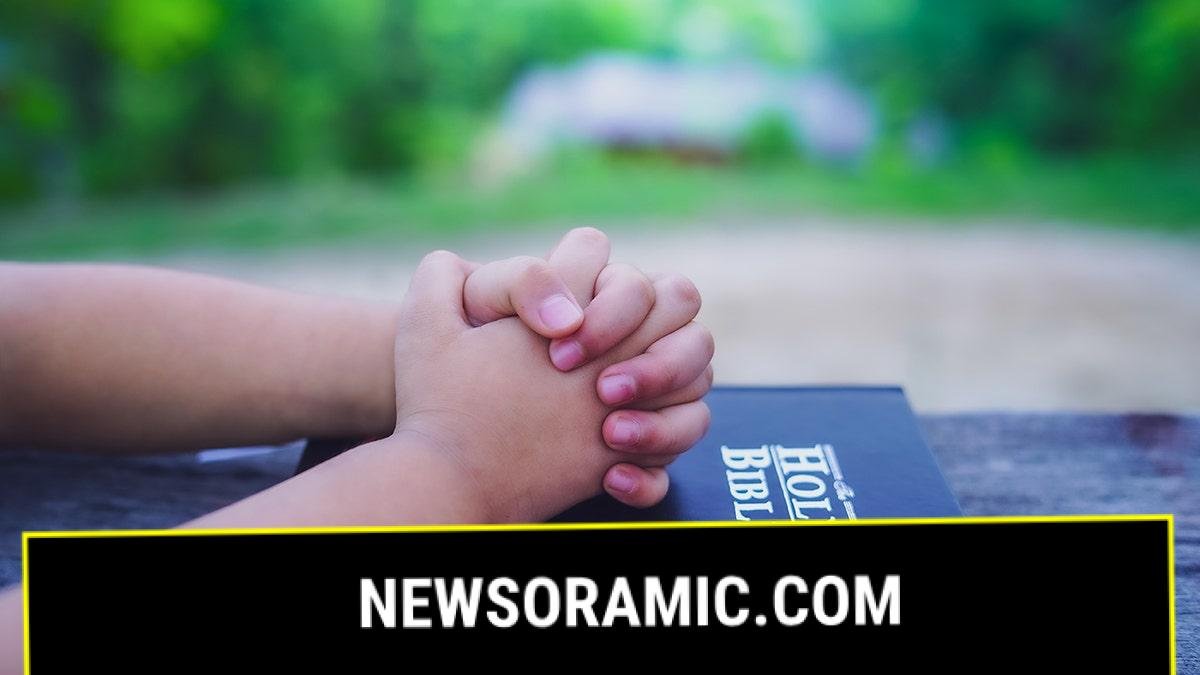Child praying with hands over Bible