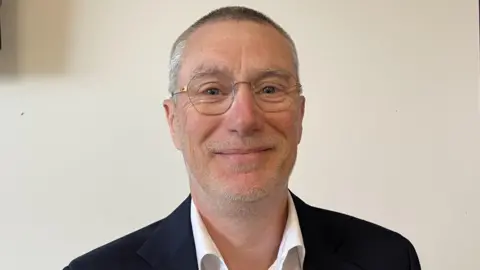 A man in a dark jacket wearing glasses