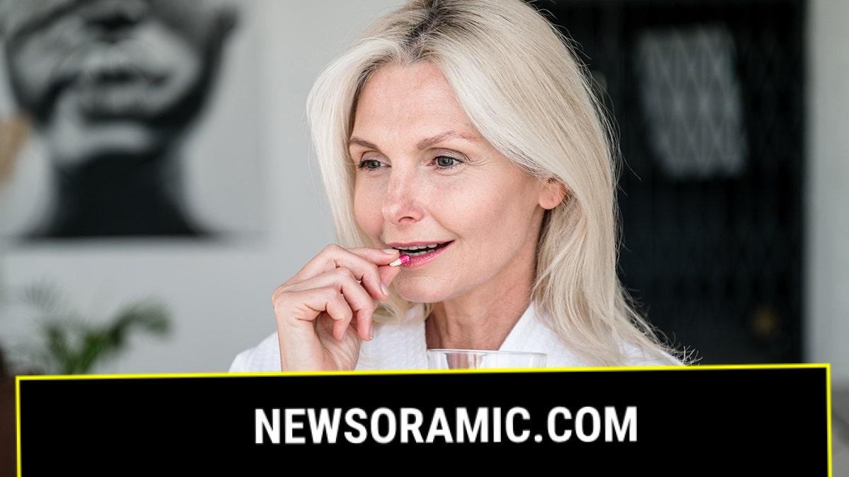 woman puts pill in her mouth holding glass of water
