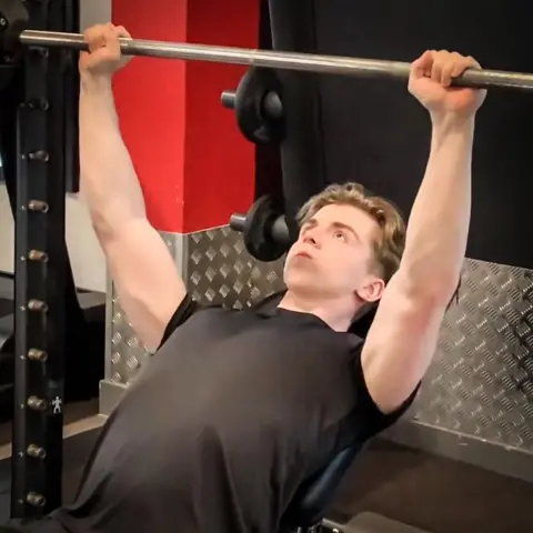 George Hazard George Hazard a boy in a black t-shirt is pushing up a barbell weight while laying on a bench, carrying out bench presses