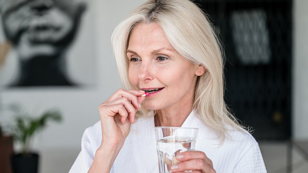 woman puts pill in her mouth holding glass of water