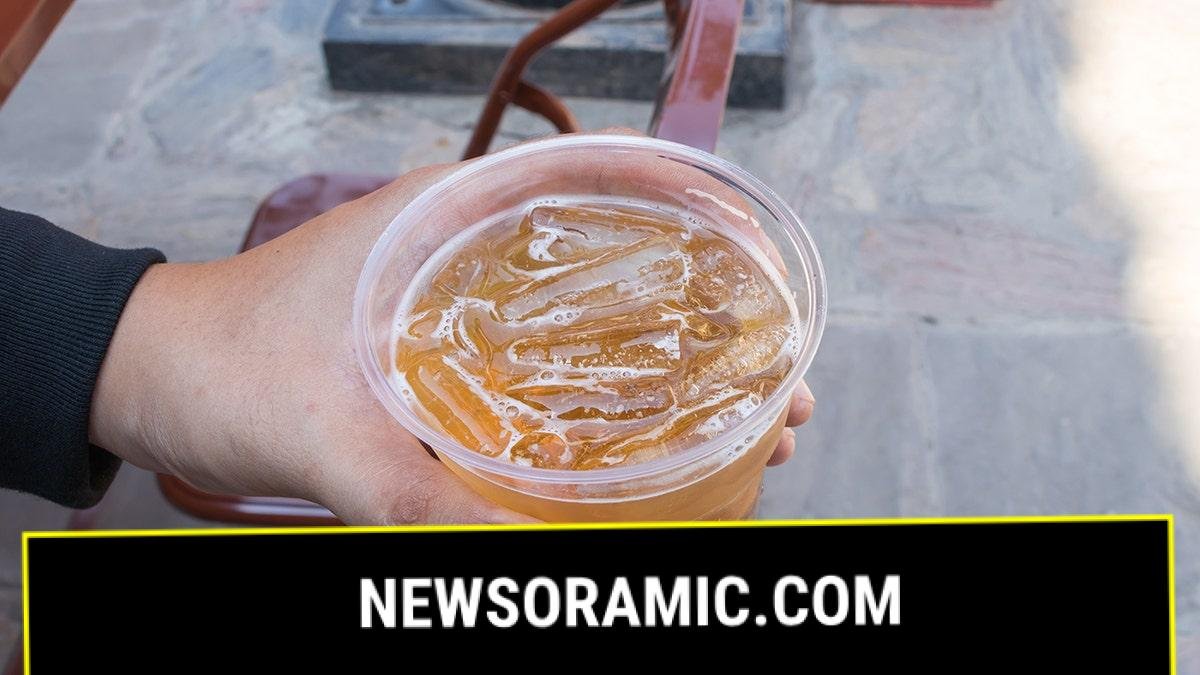 Man holding plastic cup of beer with ice in it, seen up close from above, in outdoor restaurant setting, highlighting new social media trend among Generation Z drinkers
